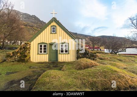 Vue sur l'église sereine de Hofskirkja, une structure pittoresque avec un toit en herbe et une croix blanche, nichée dans les douces collines herbeuses, Hofskirkja, Nordaustu Banque D'Images