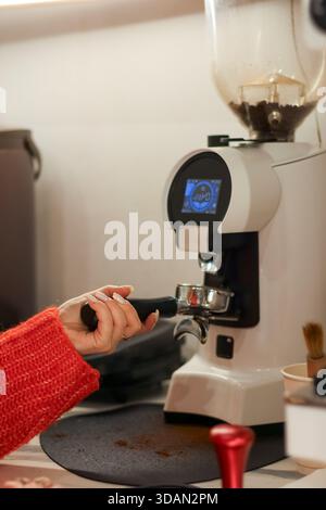 Vue rapprochée de la femme broyant des grains de café frais dans le support en métal à la station de café Banque D'Images