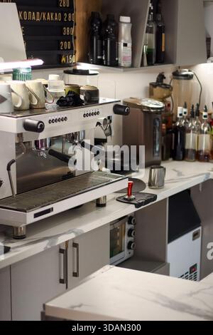 Comptoir de café bien équipé affichant machine à expresso, distributeur d'eau chaude, bouteilles de sirops, tasses et autres articles de cuisine sur une surface en marbre. Banque D'Images