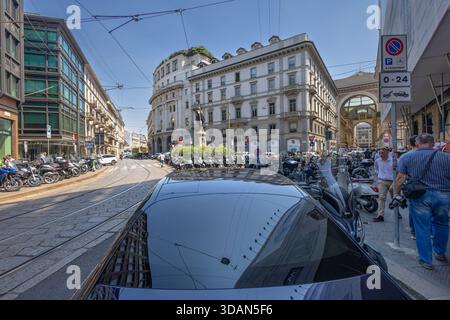 MILAN, ITALIE, 06.19.2025 :Une scène urbaine animée avec des motos garées, des rails de tramway et un grand bâtiment historique avec une arche. Piétons min Banque D'Images