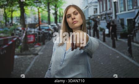 Jeune femme blonde se tient au milieu des vélos garés sur la rue pavée étroite retournant le majeur ; défi. Banque D'Images