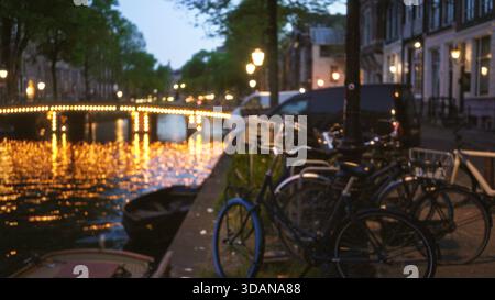 Vélos garés le long d'un canal avec des lumières de nuit floues reflétant sur l'eau à amsterdam pays-bas montrant un effet bokeh fournissant un ur tranquille Banque D'Images