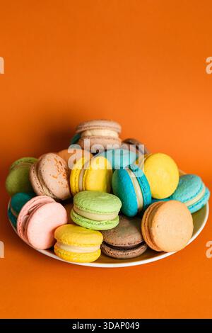 Grande assiette ronde pleine de macarons colorés sur un fond Uni orange Banque D'Images