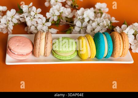 Beaucoup de macarons classiques sur des plats blancs, sur un fond orange à la lumière naturelle Banque D'Images