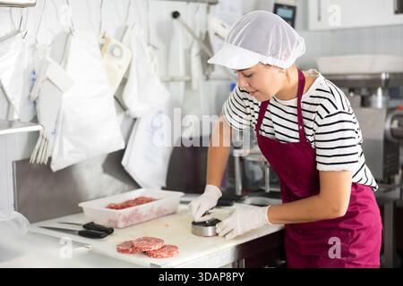 Cuisson des produits semi-finis - fille prépare les côtelettes de viande à l'aide de dispositifs spéciaux Banque D'Images