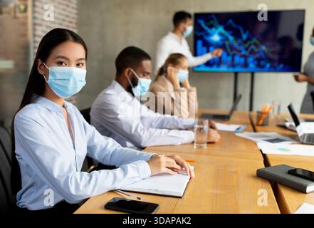 Réunion d'affaires avec divers membres de l'équipe portant des masques médicaux dans un cadre d'entreprise Banque D'Images