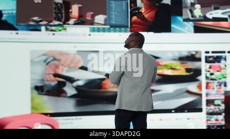 L'homme se tient devant un mur vidéo numérique entouré de vidéos en streaming et de clips de médias sociaux. L'utilisateur accède instantanément à des milliers d'options de divertissement via le tableau de bord multimédia, la caméra A. Banque D'Images