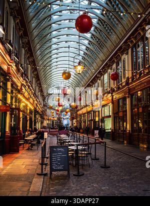 Leadenhall Market à Londres est décoré pour Noël avec de grandes boules et lumières. Les gens dînent à des tables en plein air. Banque D'Images