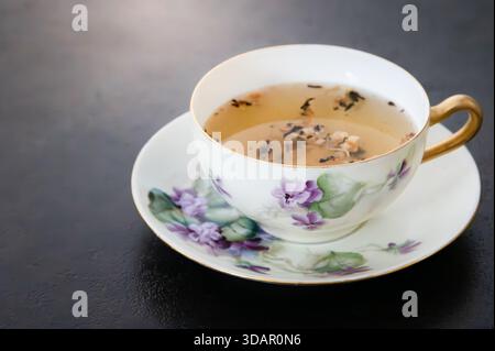 Tasse et soucoupe peintes avec des fleurs de lilas violettes, fond sombre Banque D'Images