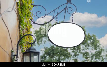 Un panneau extérieur vierge accroché sur le côté d'un bâtiment dans un endroit extérieur avec un ciel bleu, le panneau est de forme ronde. Banque D'Images