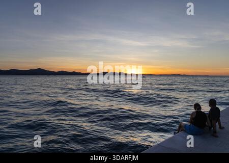 Zadar, Croatie - 17 septembre 2025 : couple assis dans les escaliers avec un orgue de mer sur le front de mer de Zadar, profitant de la côte Adriatique Banque D'Images