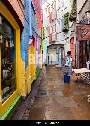 Londres, Royaume-Uni, 23 novembre 2025 : femme marchant le long d'une rue pavée humide bordée de bâtiments colorés dans la cour de neal. Londres United Kin Banque D'Images