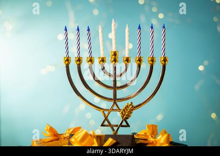 Une menorah dorée avec neuf bougies éteintes et des noeuds cadeaux jaunes est affichée sur un fond bleu vif pour Hanukkah. Banque D'Images