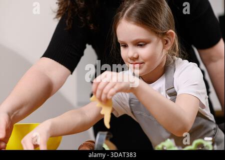 L'enfant et la mère découpent les biscuits de la pâte et les déposent sur une plaque à pâtisserie. Préparation de desserts familiaux. Banque D'Images