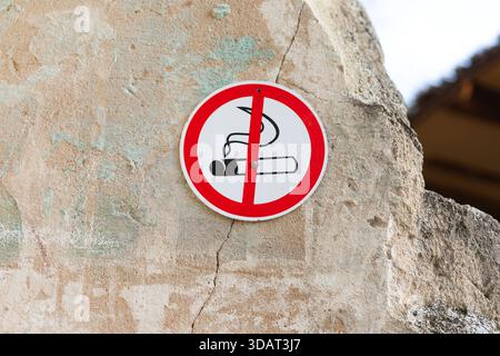 Gros plan d'un panneau d'interdiction de fumer sur un mur de pierre altérée à l'extérieur, mettant l'accent sur une zone sans fumée et les règlements de sécurité sanitaire. Banque D'Images