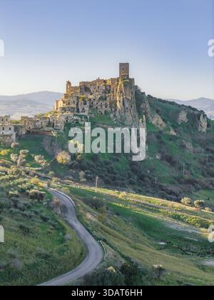 Vue aérienne de l'ancienne ville fantôme de Craco, une tapisserie de bâtiments en pierre en ruine accrochés à une falaise abrupte, baignée dans la lueur chaude du sett Banque D'Images