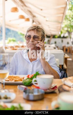Femme senior avec des lunettes parlant au téléphone au restaurant turc Banque D'Images