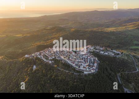 Vue aérienne d'un village perché se prélasser dans la lueur chaude du soleil couchant, avec un littoral lointain scintillant à l'horizon, Rotondella, Basilique Banque D'Images