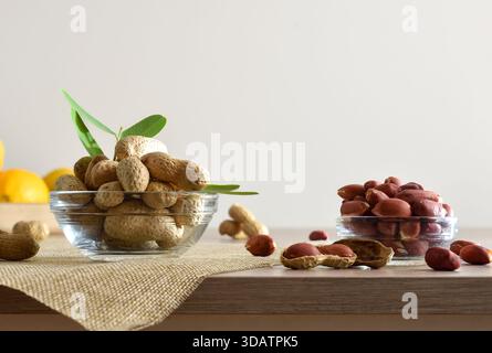 Cacahuètes pelées et non pelées dans des bols en verre sur un banc de cuisine en bois et fond isolé blanc. Vue de face. Banque D'Images