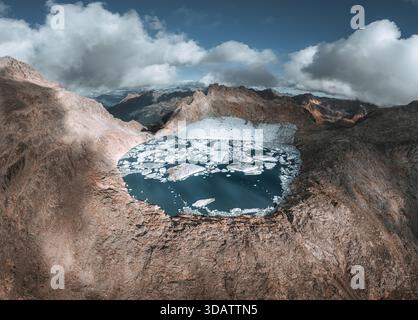 Vue des icebergs à la dérive dans le lac glaciaire, bercé par des montagnes escarpées sous un ciel brossé de nuages, Bedretto, Tessin, Suisse. Banque D'Images