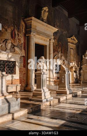 Pise, Italie - 26 juin 2025 : la galerie est du Camposanto monumentale, montrant des tombes de marbre, des bustes sculptés, et l'entrée de la Cappella Dal Banque D'Images