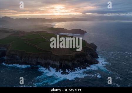 Vue aérienne des champs verdoyants rencontrant la côte accidentée alors que les vagues s'écrasent contre les falaises, Ribeirinha, Açores, Portugal. Banque D'Images