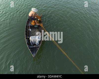 Vue aérienne d'un pêcheur solitaire dans un bateau étroit, jetant un long filet jaune dans les eaux vertes chatoyantes, Hội an, Quảng Nam, Vietnam. Banque D'Images