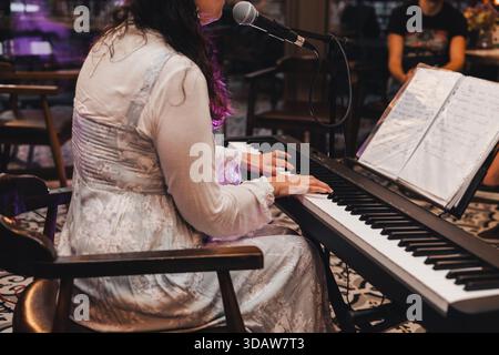 Femme méconnaissable recadrée se produit lors d'un concert, jouant d'un clavier électronique et chantant dans un microphone, avec des partitions sur un stand, de la créatine Banque D'Images