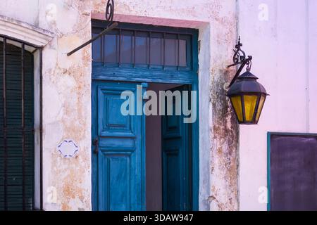 Une porte en bois bleu vif avec une lanterne rustique orne un vieux mur texturé à Colonia del Sacramento, Uruguay, mettant en valeur le charmant colon de la ville Banque D'Images