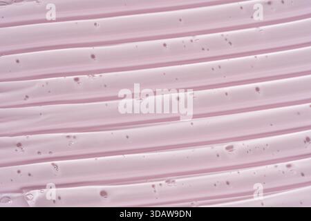 Image en gros plan de la texture lisse du sérum de gel cosmétique rose, présentant un motif de lignes parallèles. Le fond rose pâle rehausse le délicat et le c Banque D'Images