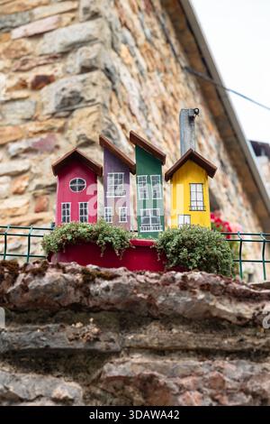 Une charmante collection de maisons miniatures en bois colorées est perchée sur un mur de pierre orné de plantes vertes, dans le cadre rustique de la Banque D'Images