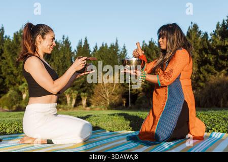 Deux femmes se baignent dans un bain sonore avec des bols chantants tibétains dans le plein air serein de la Nouvelle-Zélande pendant l'automne, entourées de verdure luxuriante et de tran Banque D'Images