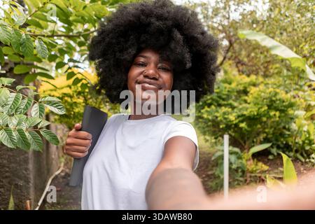 Femme afro-américaine avec un afro apprécie la verdure luxuriante de Bali, embrassant le mode de vie nomade numérique. Souriante et tenant un ordinateur portable, elle me trouve Banque D'Images