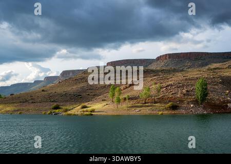 Belle vue sur le lac Akkoy Dam en Turquie, entouré de collines rocheuses et d'arbres verts vibrants sous un ciel spectaculaire rempli de nuages sombres et roulants an Banque D'Images