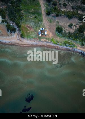Image aérienne montrant des camping-cars garés sur une plage isolée et sauvage. La scène capture les vagues de l'océan sereines, les rives sablonneuses intactes et les environs Banque D'Images