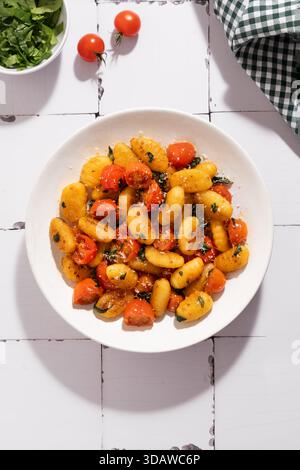 Vue de dessus de délicieux gnocchi avec tomates cerises et épinards sur une assiette blanche, placée sur un fond en bois rustique. Épinards frais et tomates acco Banque D'Images
