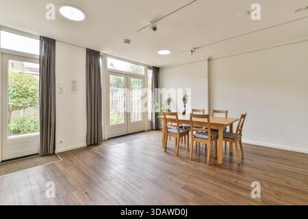 Une salle à manger spacieuse avec un mobilier en bois, de grandes fenêtres permettant la lumière naturelle, et une esthétique minimaliste. Idéal pour les réunions de famille et inti Banque D'Images