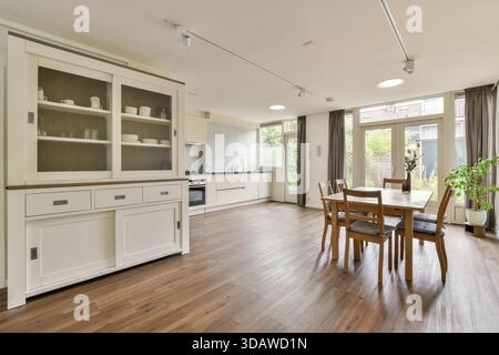 La salle à manger lumineuse et spacieuse dispose de parquet, d'armoires élégantes et d'une lumière naturelle abondante, créant une atmosphère accueillante pour les repas. Banque D'Images