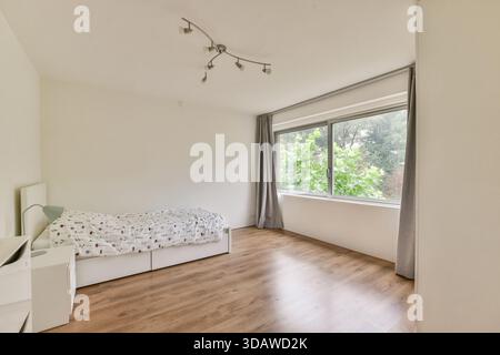 Une chambre contemporaine au design minimaliste avec une lumière naturelle abondante diffusant à travers de grandes fenêtres, créant une atmosphère accueillante. Banque D'Images