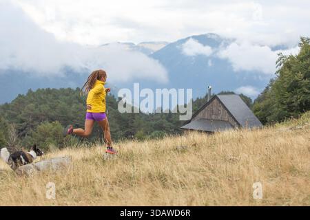 Une femme en vêtements de sport vibrants court joyeusement le long d'un sentier de montagne pittoresque avec son chien énergique à côté d'elle, embrassant la beauté et la liberté de Outdo Banque D'Images