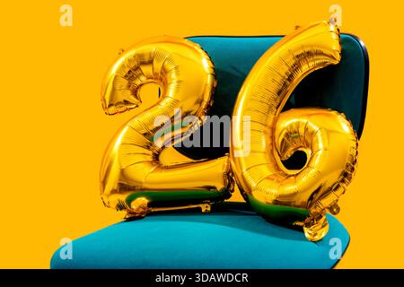 Les ballons en aluminium doré brillants en forme de numéros deux et six créent une atmosphère festive sur un fond orange vif, incarnant l'esprit de Banque D'Images