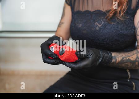Une femme tatoueuse avec des tatouages sur ses bras porte des gants noirs, prépare des outils pour une séance de tatouage, créant un professionnel et créatif à Banque D'Images