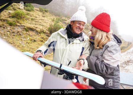 Un couple plus âgé, chaudement vêtu de vêtements d'hiver, partage un moment joyeux à l'extérieur tout en se préparant aux activités hivernales, capturant l'essence d'un Banque D'Images