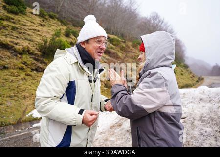 Un couple plus âgé partage joyeusement un moment à l'extérieur, habillé chaudement contre le froid hivernal. Leurs sourires et leur interaction capturent l'essence du plaisir Banque D'Images