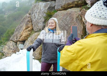 Un couple âgé joyeux embrasse le temps froid, se livrant à des activités hivernales au milieu d'un terrain rocheux et de la neige, capturant des souvenirs avec un sens Banque D'Images