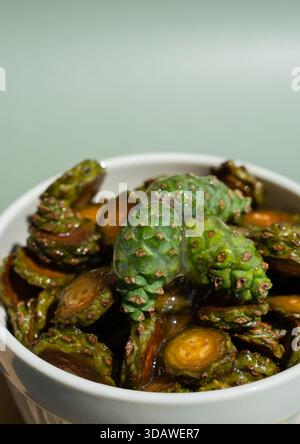 Un bol de miel de pommes de pin bio avec des pommes de pin vertes immergées dans du sirop, sur un fond vert doux. Le bol en céramique améliore le naturel Banque D'Images