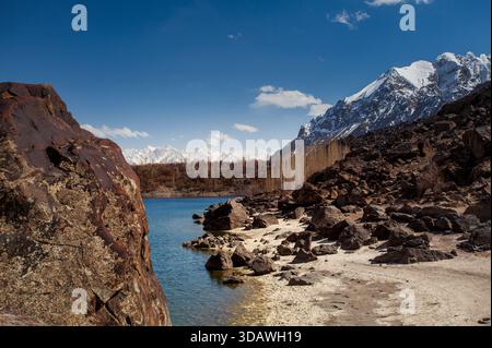Vue des eaux Azur reflétant le ciel dégagé, embrassées par des rivages rocheux menant aux montagnes enneigées à Kachura, Skardu, Pakistan. Banque D'Images
