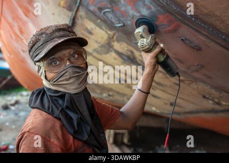 Dhaka, Bangladesh - 31 août 2024 : vue d'un travailleur qui grince le côté d'un bateau, étincelle volant sous le soleil, réfléchissant sur les lunettes de sécurité Banque D'Images