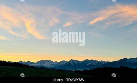 Lever de soleil matinal d'hiver unique derrière une imposante chaîne de montagnes aux tons jaunes chauds et au ciel doux dans les Alpes suisses, Oberland bernois, Suisse Banque D'Images