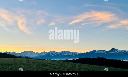 Lever de soleil matinal d'hiver unique derrière une imposante chaîne de montagnes aux tons jaunes chauds et au ciel doux dans les Alpes suisses, Oberland bernois, Suisse Banque D'Images